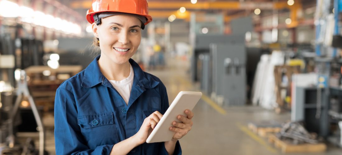 Young successful female engineer of large industrial plant surfing in the net while standing in front of camera